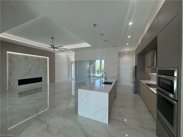 Kitchen featuring a center island with sink, sink, a tray ceiling, gray cabinets, and pendant lighting