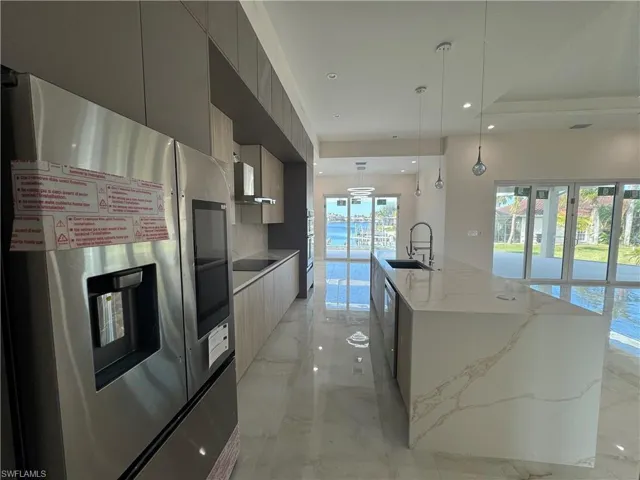Kitchen featuring appliances with stainless steel finishes, gray cabinetry, sink, decorative light fixtures, and an island with sink