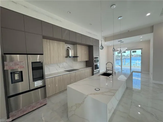 Kitchen featuring appliances with stainless steel finishes, light brown cabinetry, sink, pendant lighting, and a center island with sink