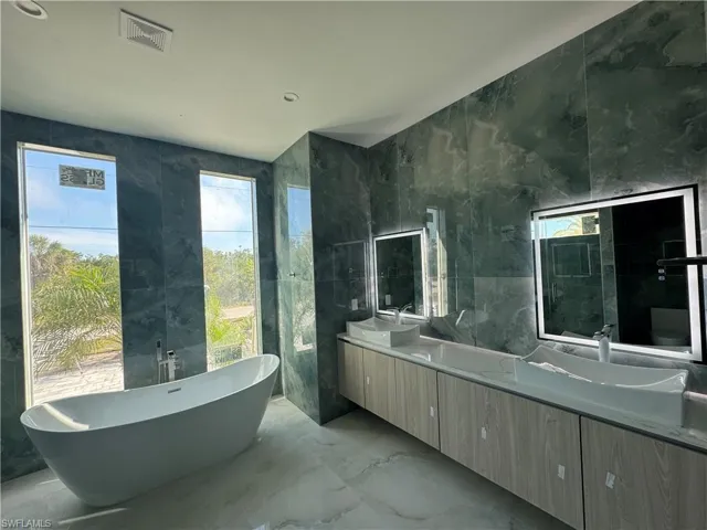Bathroom with vanity, a tub to relax in, and tile walls