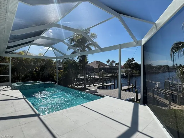 View of pool with glass enclosure, a water view, a patio area, a boat dock, and an in ground hot tub