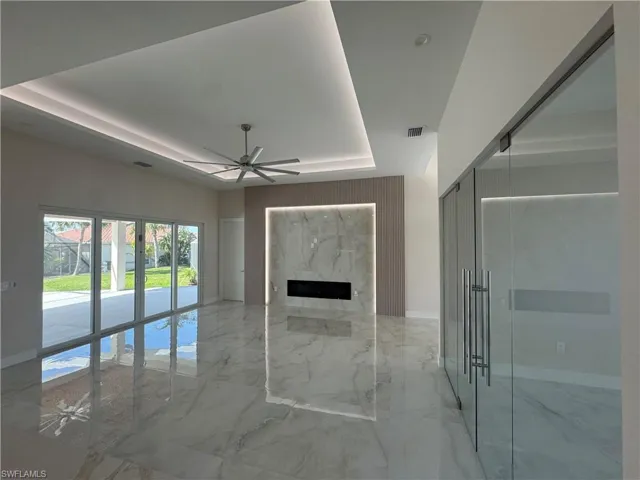 Unfurnished living room with a high end fireplace, ceiling fan, and a raised ceiling