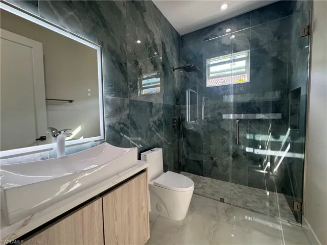 Bathroom with vanity, toilet, walk in shower, and tile walls