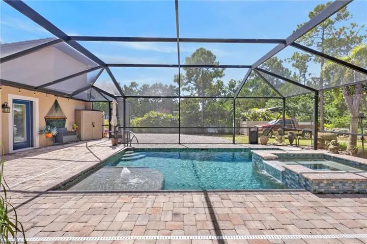 Screened enclosure featuring a swimming pool, integrated spa, paver patio, and exterior door access