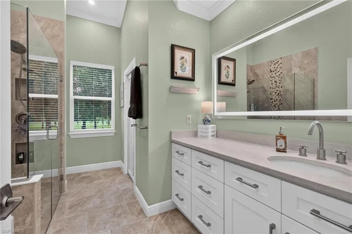 Spacious bathroom featuring a dual vanity with undermount sinks, an expansive illuminated mirror, a glass-enclosed shower with tile surround, and large format floor tile