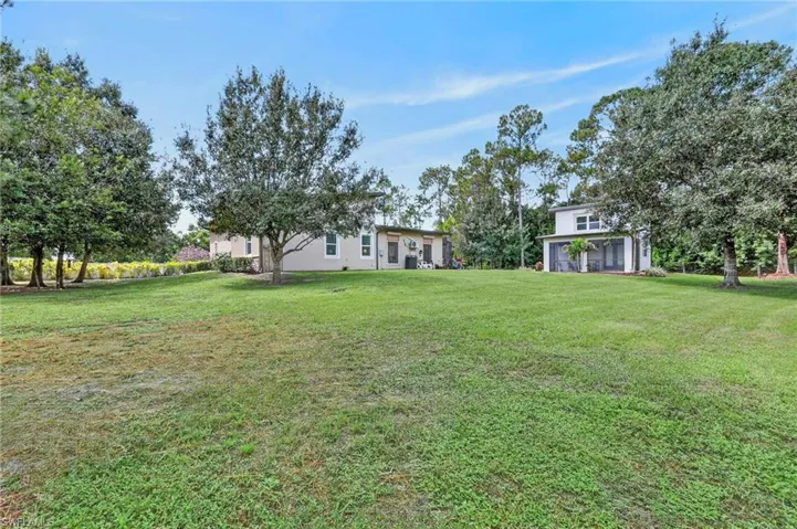 Expansive green lawn with mature trees and a two-story residence featuring a screened patio