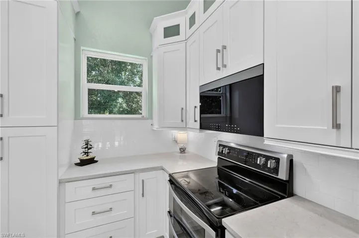 White shaker cabinetry with brushed nickel hardware, light-toned countertops, subway tile backsplash, built-in microwave, and a black electric range