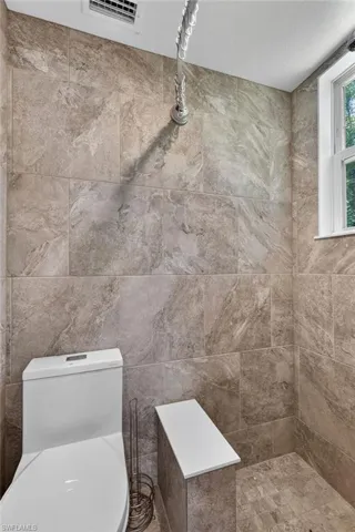 Floor-to-ceiling tile in the shower, a built-in shower bench, and a window for natural light