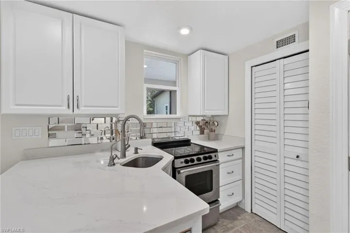 Modern kitchen featuring white shaker-style cabinetry, a white quartz countertop with waterfall edge detail, stainless steel gas range with black accents, an undermount sink with chrome faucet, and a geometric tile backsplash