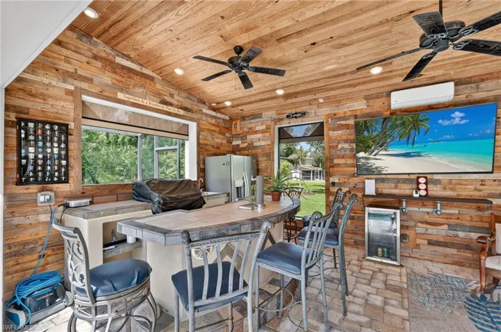 Vaulted wood-paneled ceiling, wood plank wall finishes, integrated wet bar with tile countertop, built-in outdoor kitchen with sink, and paver flooring