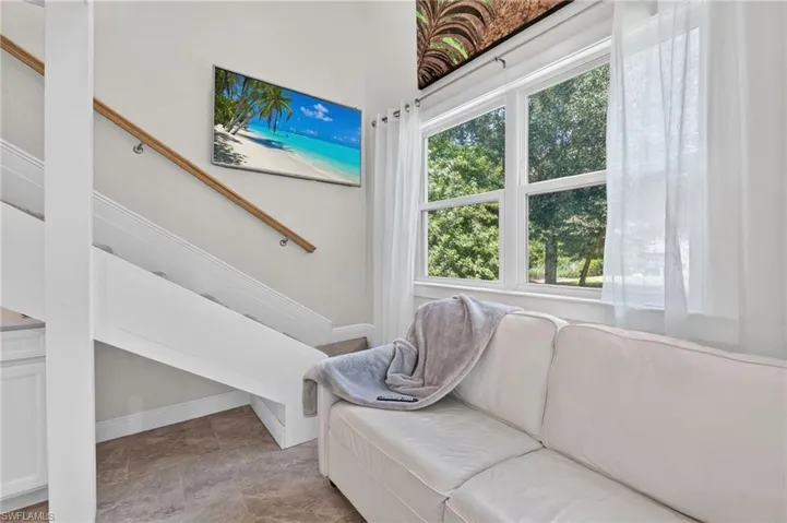 White staircase with a wood-finish handrail, multi-pane window, and light-toned flooring