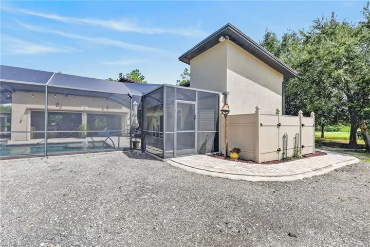 Screened-in pool enclosure, stucco exterior, paved walkway, and a privacy-fenced utility area