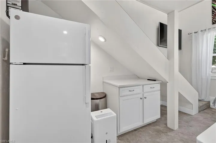 White refrigerator, recessed ceiling lighting, light-toned flooring, white cabinetry with silver-tone hardware, and an interior staircase