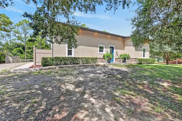 Stucco exterior with stone accenting, a vibrant blue entry door, manicured shrubbery, and mature trees