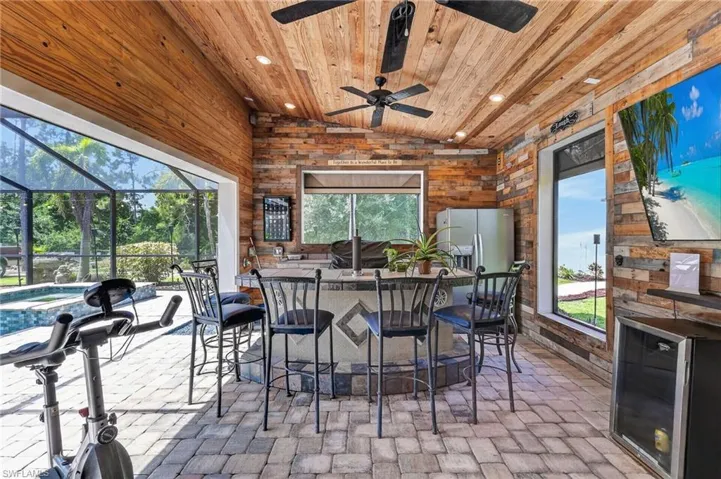 Screened lanai featuring wood-finish ceiling with recessed lighting, ceiling fans, paver flooring, and a built-in bar with stone countertop