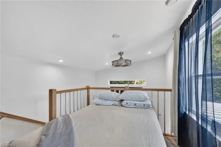 Loft space featuring a wood-finish railing, vaulted ceiling with recessed lighting, and a window with sheer drapery
