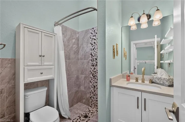 Guest Bathroom with a shower featuring stone-look tile and mosaic accents, a vanity with a light-toned countertop, and a wall-mounted light fixture