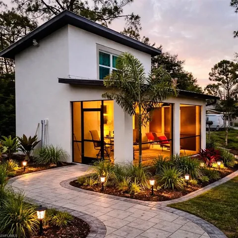 Two-story structure with stucco exterior, screened-in patio, paver pathway, landscape lighting, and established plantings