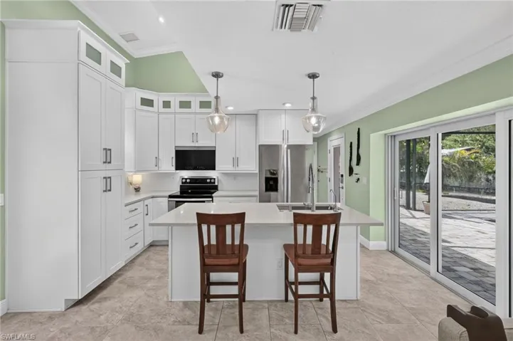 Kitchen featuring white cabinetry, a central island with countertop seating, stainless steel appliances, pendant lighting, and sliding glass doors to outdoor paving
