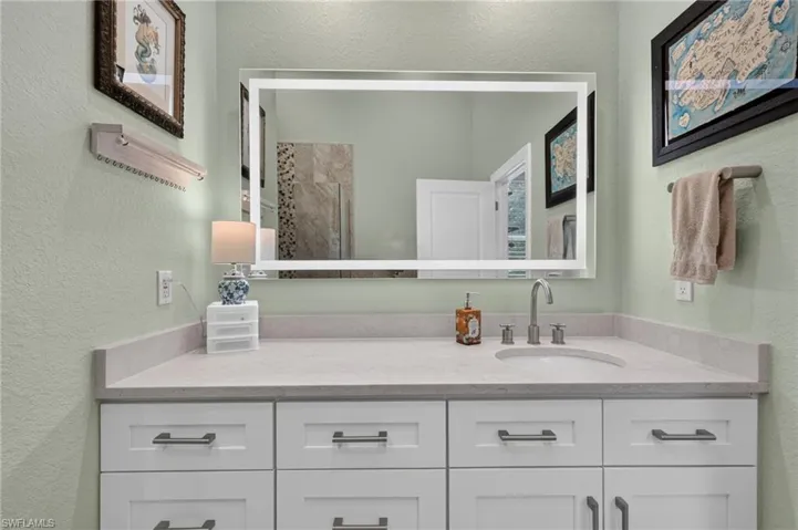 Vanity featuring white shaker-style cabinetry, a light-toned countertop, an undermount sink with a brushed nickel faucet, and an illuminated mirror