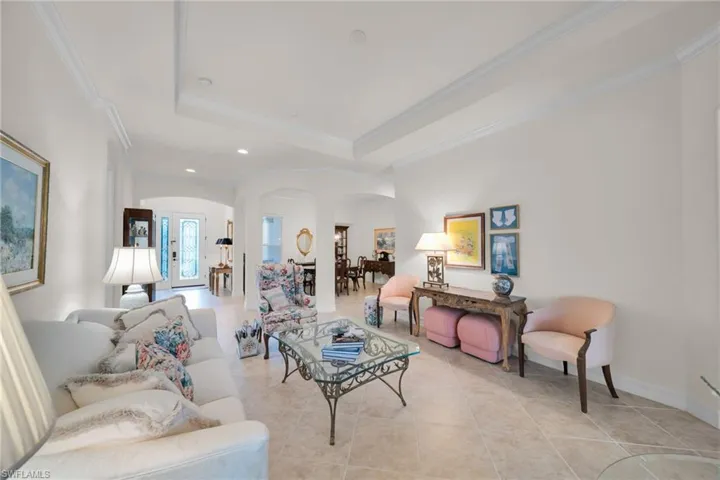 Living area featuring arched walkways, light tile patterned floors, ornamental molding, a tray ceiling, and recessed lighting