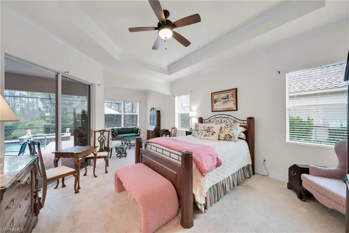 Bedroom featuring light carpet, a tray ceiling, ornamental molding, and ceiling fan