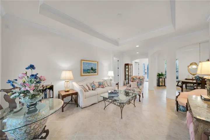 Living area with a tray ceiling, arched walkways, ornamental molding, and light tile patterned flooring