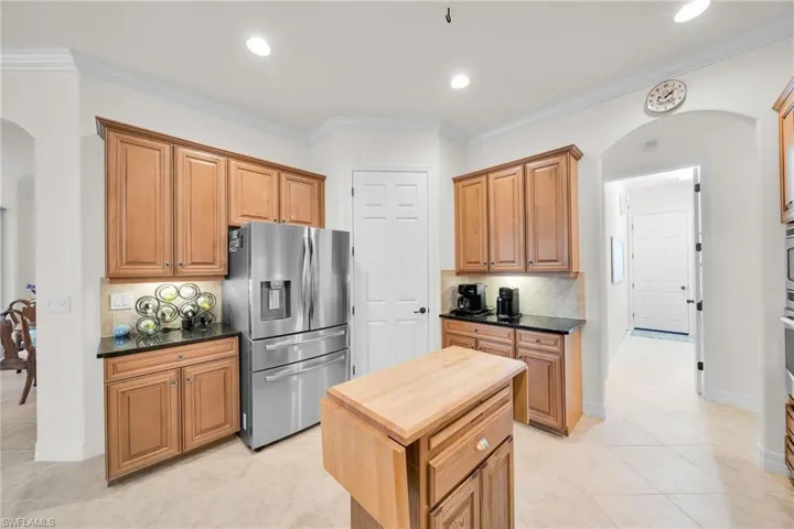 Kitchen with arched walkways, stainless steel fridge with ice dispenser, crown molding, dark stone countertops, and brown cabinets