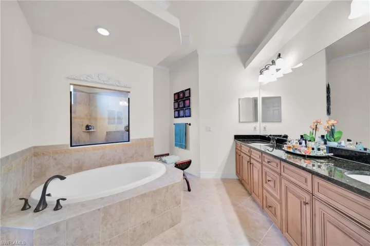 Bathroom featuring a bath, double vanity, ornamental molding, and light tile patterned floors