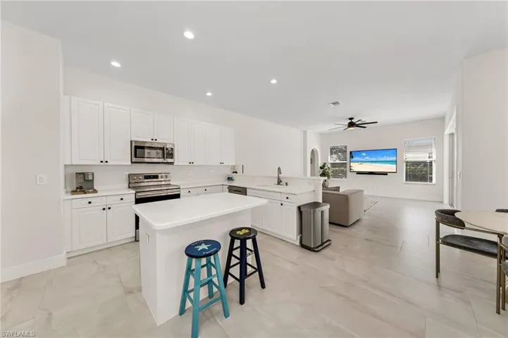 Kitchen featuring stainless steel appliances, a kitchen bar, a kitchen island, ceiling fan, and white cabinetry