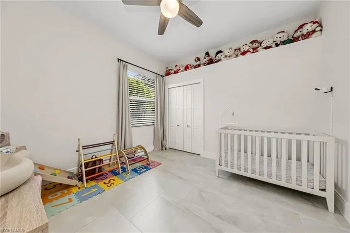 Bedroom featuring ceiling fan, a nursery area, light tile patterned flooring, and a closet