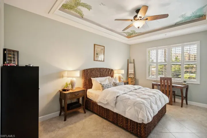 Bedroom with ornamental molding, a tray ceiling, ceiling fan, and light tile patterned floors