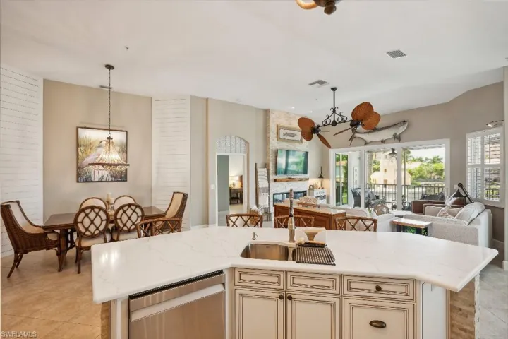 Kitchen featuring cream cabinetry, light stone countertops, decorative light fixtures, a center island with sink, and stainless steel dishwasher
