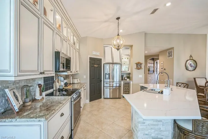 Kitchen featuring appliances with stainless steel finishes, light stone counters, an island with sink, decorative light fixtures, and sink