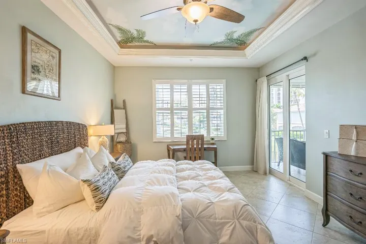 Tiled bedroom with access to outside, a tray ceiling, multiple windows, and ceiling fan