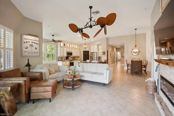Living room with ceiling fan with notable chandelier, vaulted ceiling, light tile patterned floors, and a fireplace