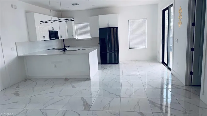 Kitchen with light tile floors, black appliances, white cabinetry, light stone counters, and a peninsula