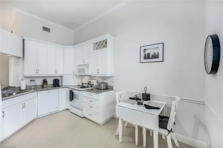 Kitchen with white appliances, sink, light stone countertops, white cabinetry, and ornamental molding