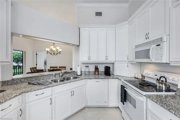 Kitchen with white cabinetry, white appliances, light stone countertops, sink, and ornamental molding