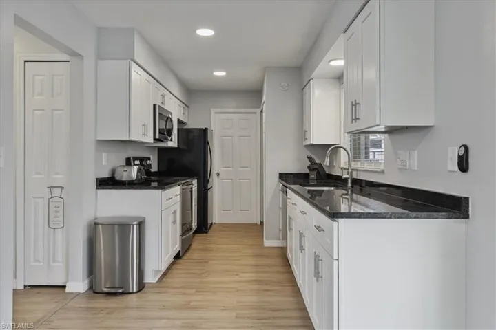Kitchen featuring stainless steel appliances, dark stone counters, white cabinets, light wood-style flooring, and recessed lighting