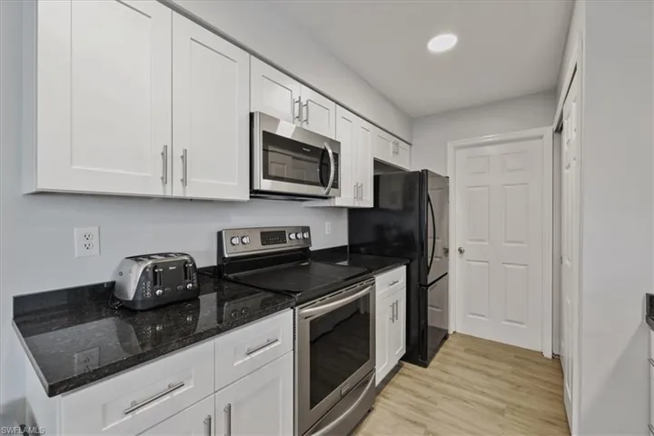 Kitchen with appliances with stainless steel finishes, dark stone countertops, white cabinetry, and light wood-type flooring