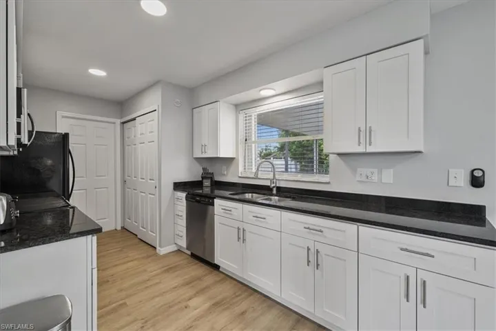 Kitchen with dark stone counters, white cabinets, stainless steel appliances, light wood finished floors, and recessed lighting