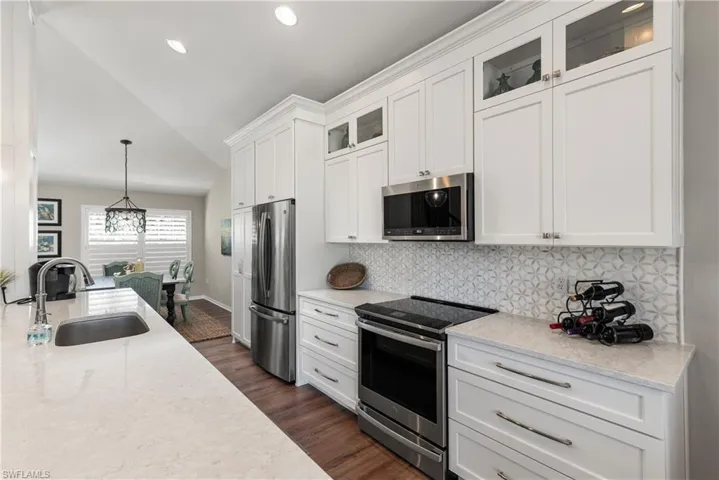 Kitchen featuring a sink, backsplash, stainless steel appliances, white cabinets, and lofted ceiling