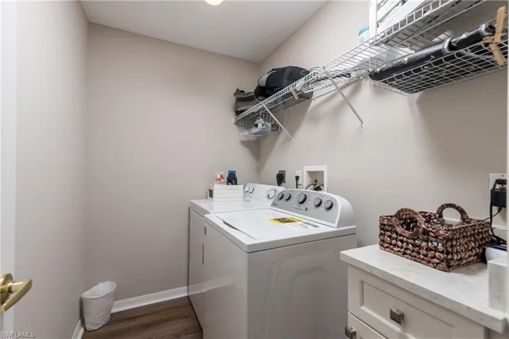 Clothes washing area featuring washing machine and clothes dryer, baseboards, and wood finished floors