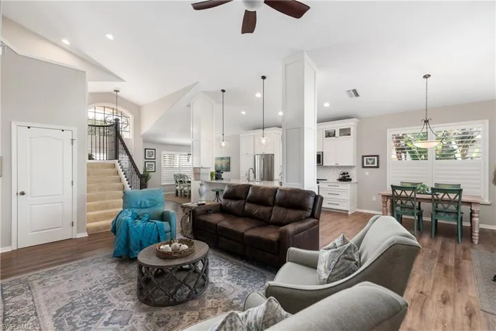 Living room with vaulted ceiling, a healthy amount of sunlight, light wood finished floors, and stairway