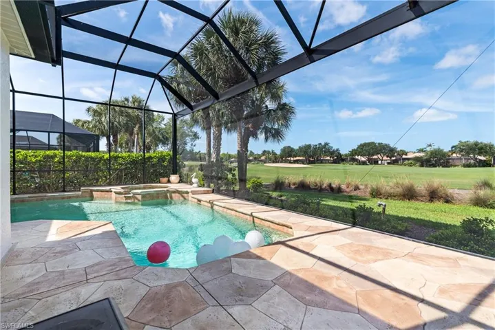 View of swimming pool featuring a lawn, glass enclosure, a pool with connected hot tub, and a patio