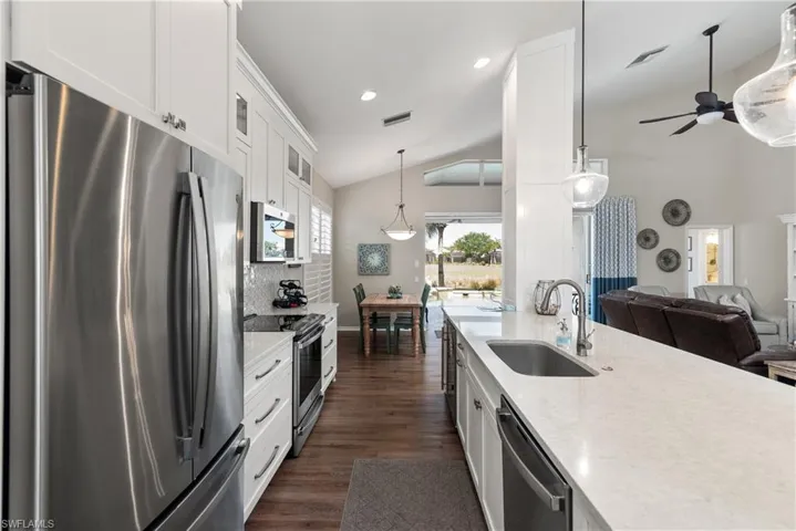 Kitchen with vaulted ceiling, a ceiling fan, a sink, glass insert cabinets, and stainless steel appliances