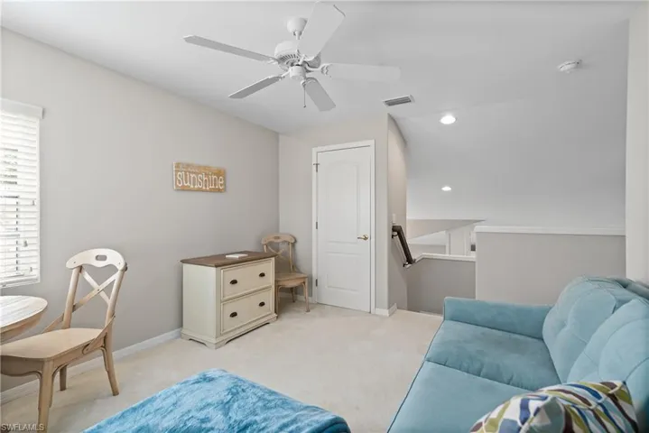 Living area with light carpet, a ceiling fan, an upstairs landing, and visible vents