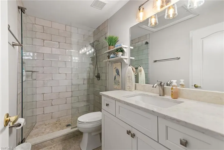 Bathroom featuring tile patterned floors, a tile shower, toilet, visible vents, and vanity