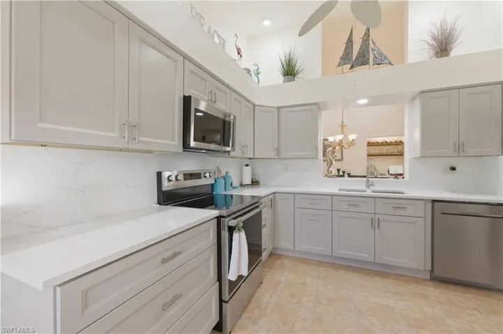 Kitchen featuring stainless steel appliances, backsplash, hanging lights, light stone countertops, and gray cabinetry